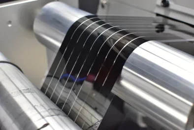 A machine processes black peel-and-stick solar panels in an industrial roll-to-roll printer